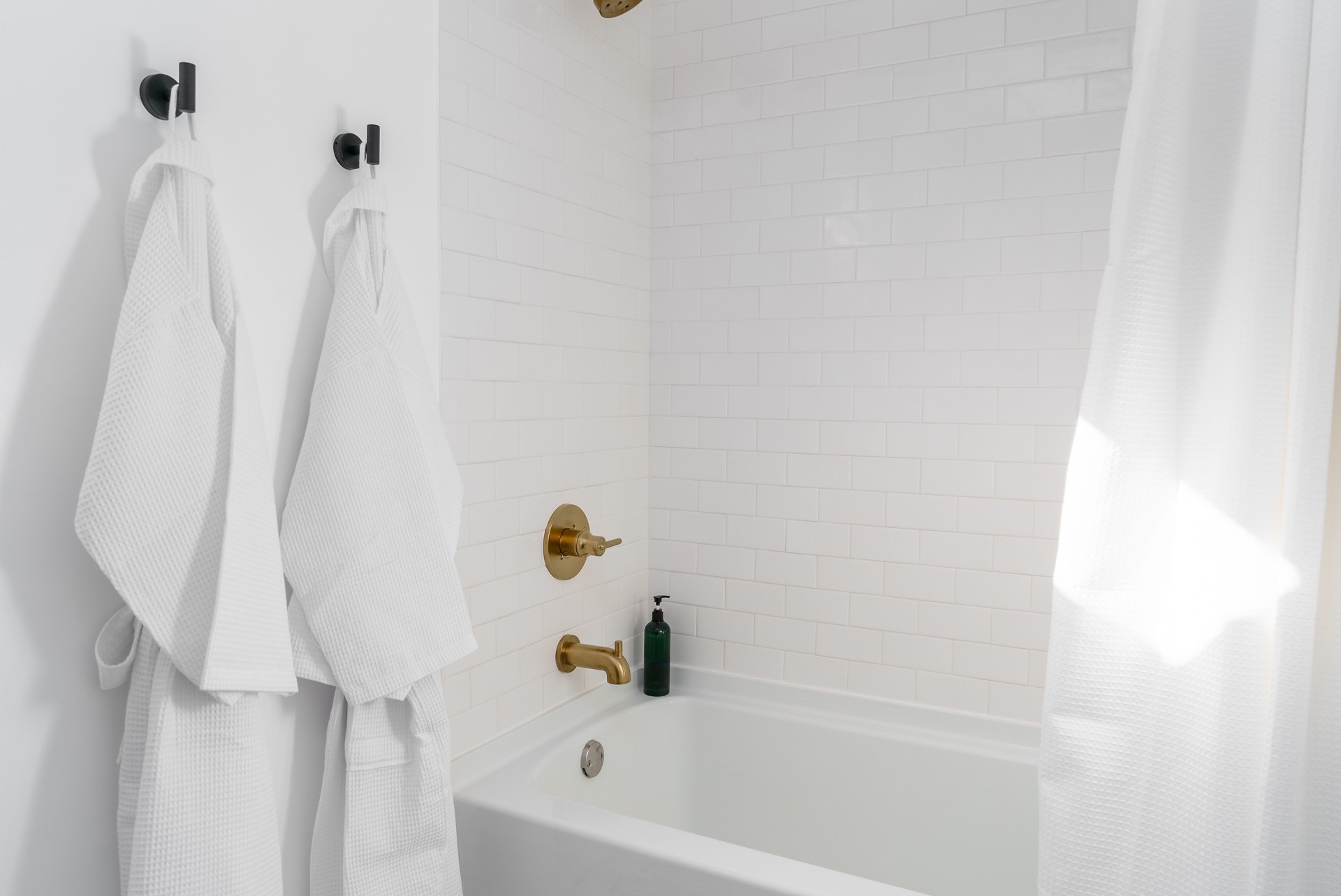 White bathroom shower tub, brass hardware, and bath robes